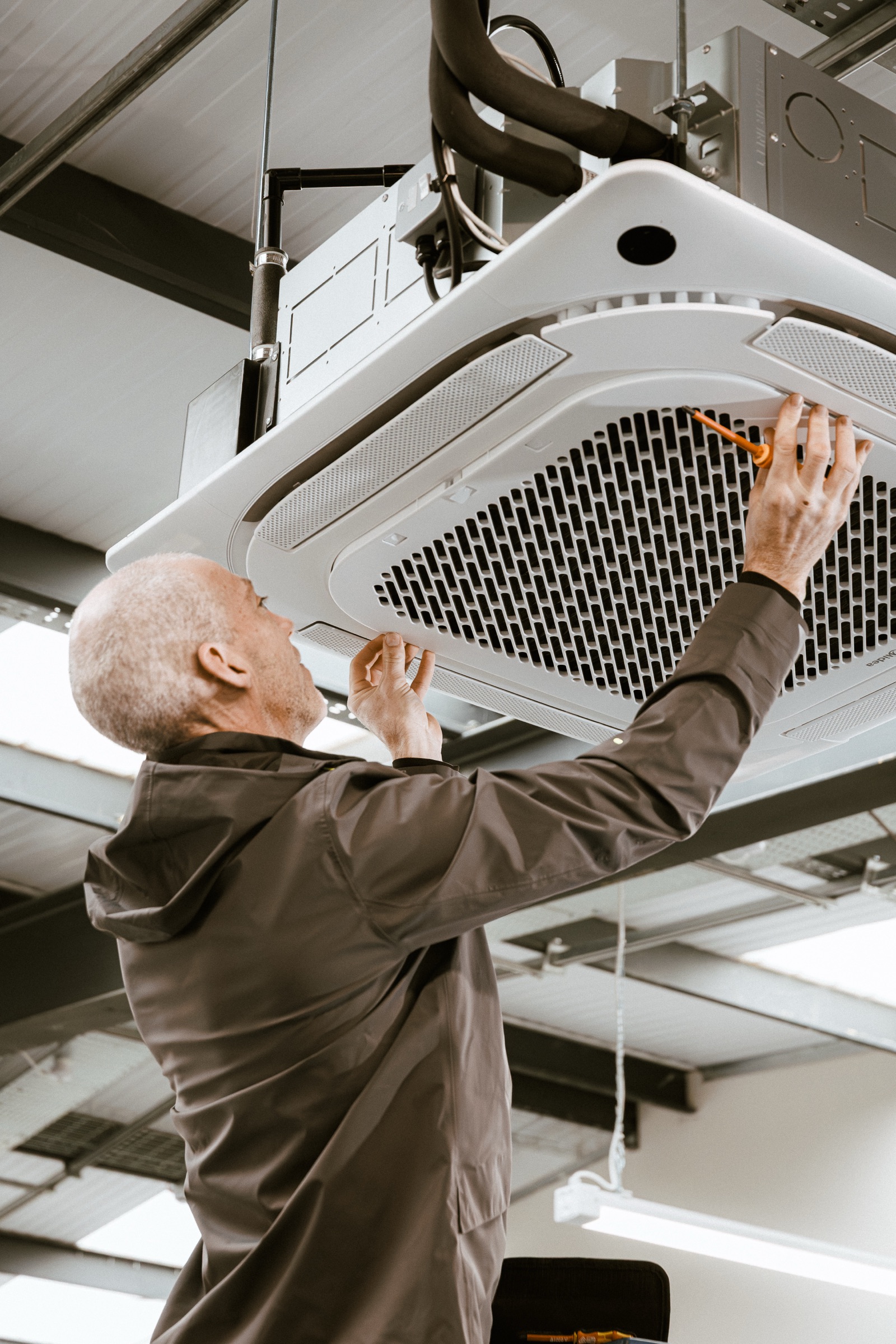 Two engineers in branded olive workwear stand together in a plant room, calm and confident, mid-conversation about an installation.